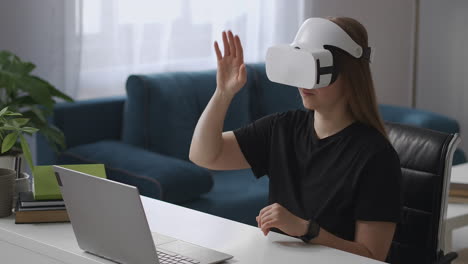 woman-is-using-vr-head-mounted-display-connected-to-laptop-viewing-display-and-screen-gesticulating-by-hands-for-control-medium-female-portrait-at-home